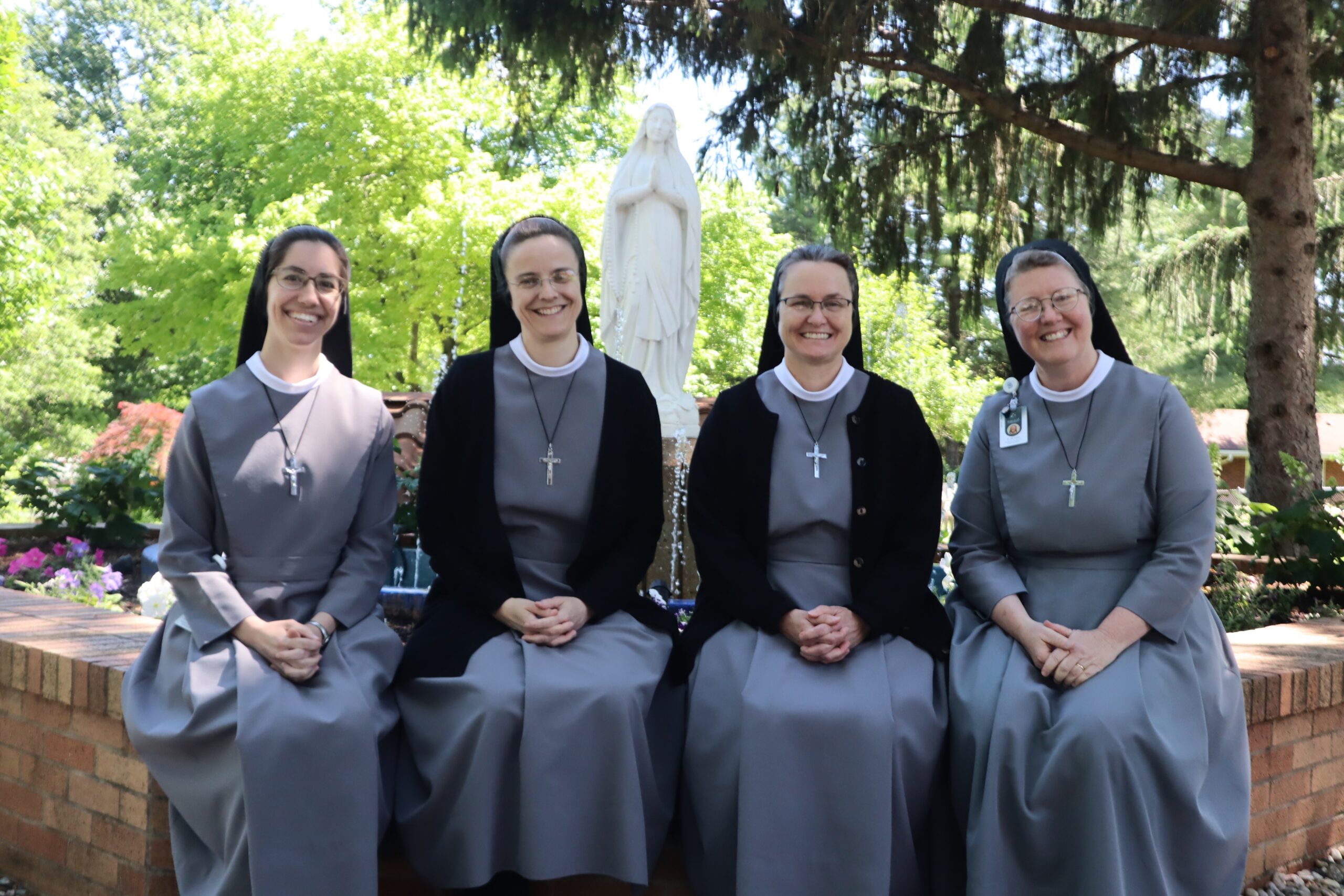 Four sisters sit posed at the Mary fountain. They are Sister M. Caterina, Sister M. Anselma, Sister M. Elena, and Sister M. Luka.