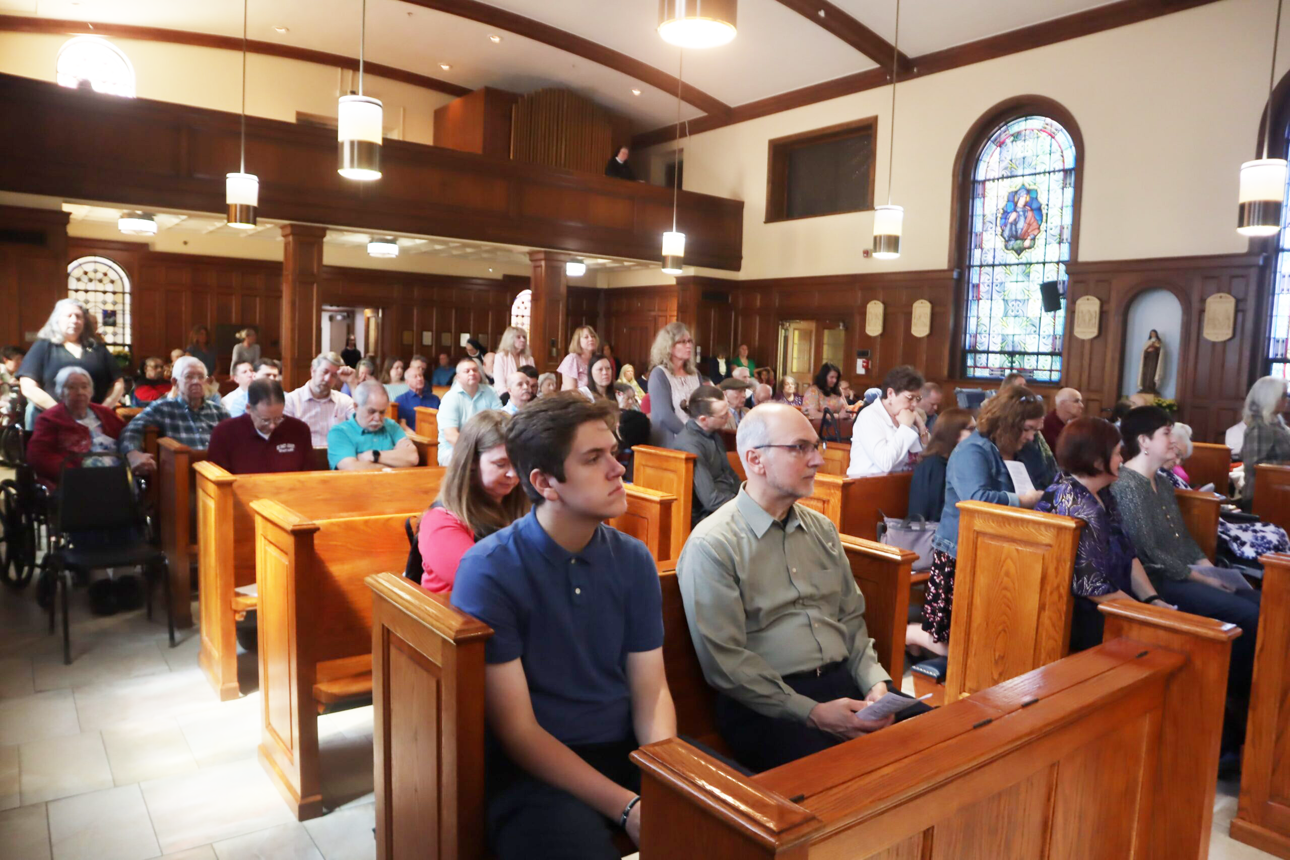 A photo of the congregation in the chapel during a Sunday mass. There are many families, friends, and residents.