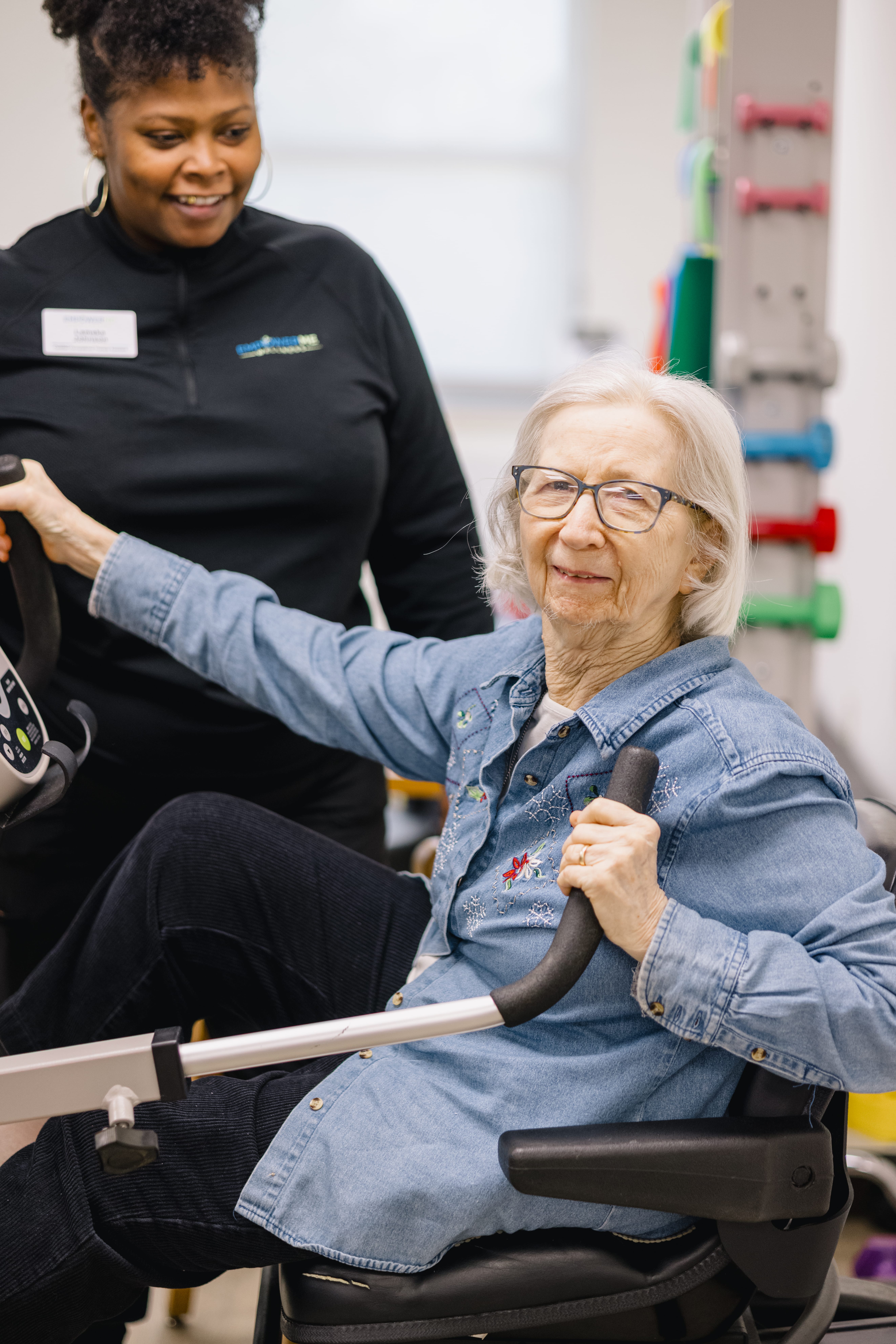 A resident using physical therapy equipment in the therapy room, with a physical therapist.