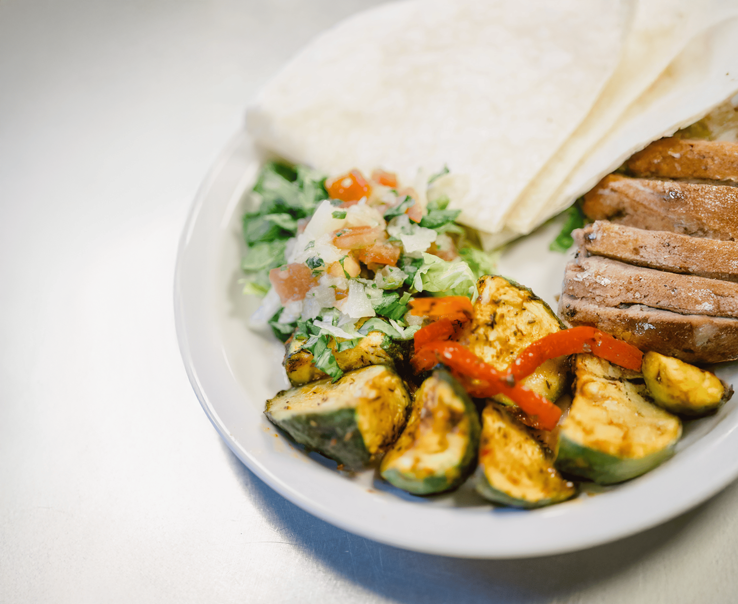 A close up photo of a resident meal made by the kitchen. There are roasted vegetables, slices of chicken, tortillas, and pico de gallo on the plate.