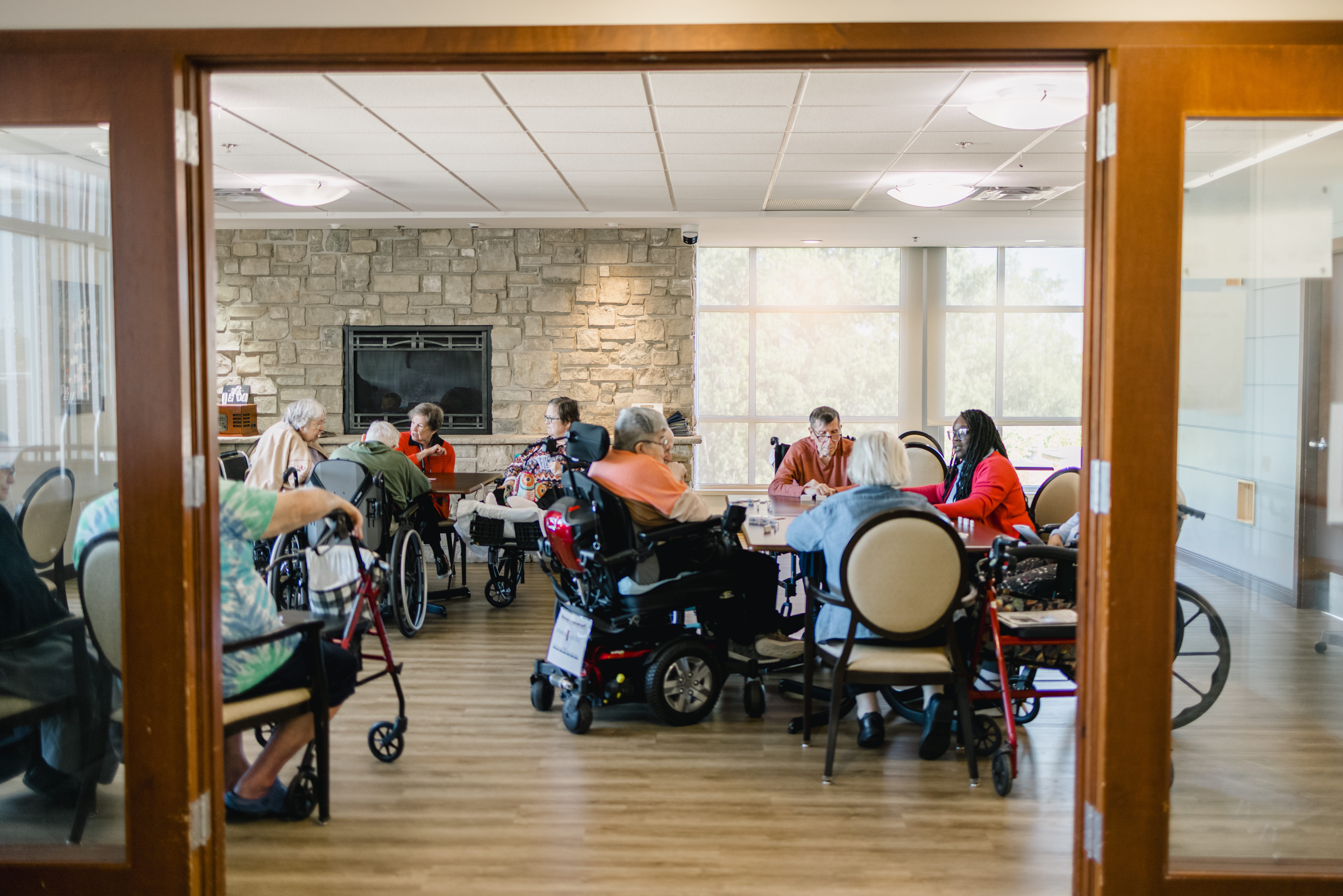 Residents and volunteers sitting in the dining room playing a game. There is a volunteer and a Mission Partner among them.