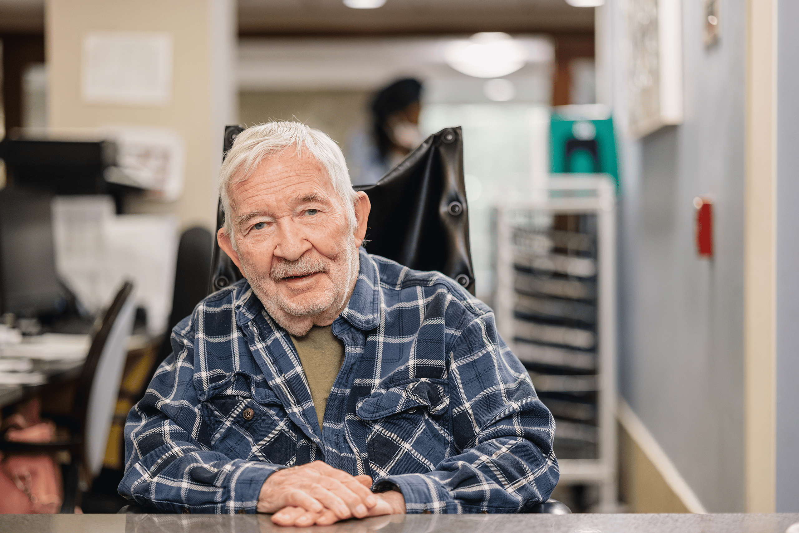A resident sitting in a wheelchair at the nurses' station smiling.