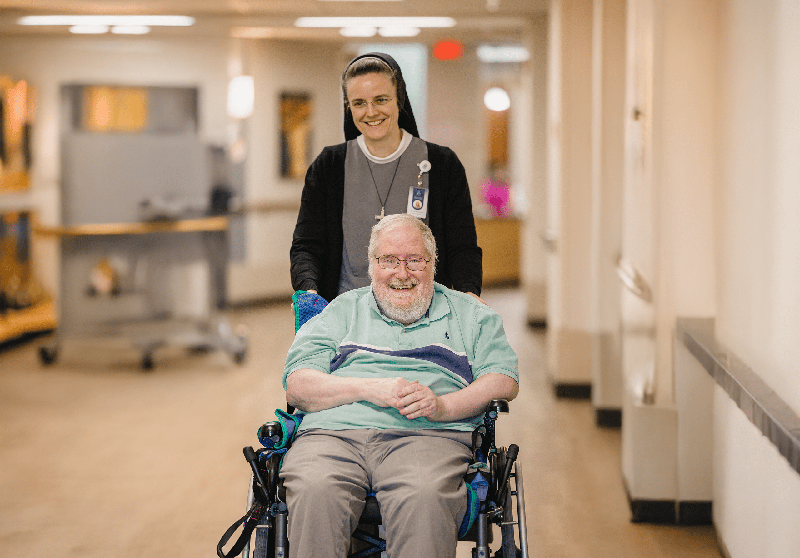 Sister M. Anselma posing with a resident in a wheelchair. Both are smiling.